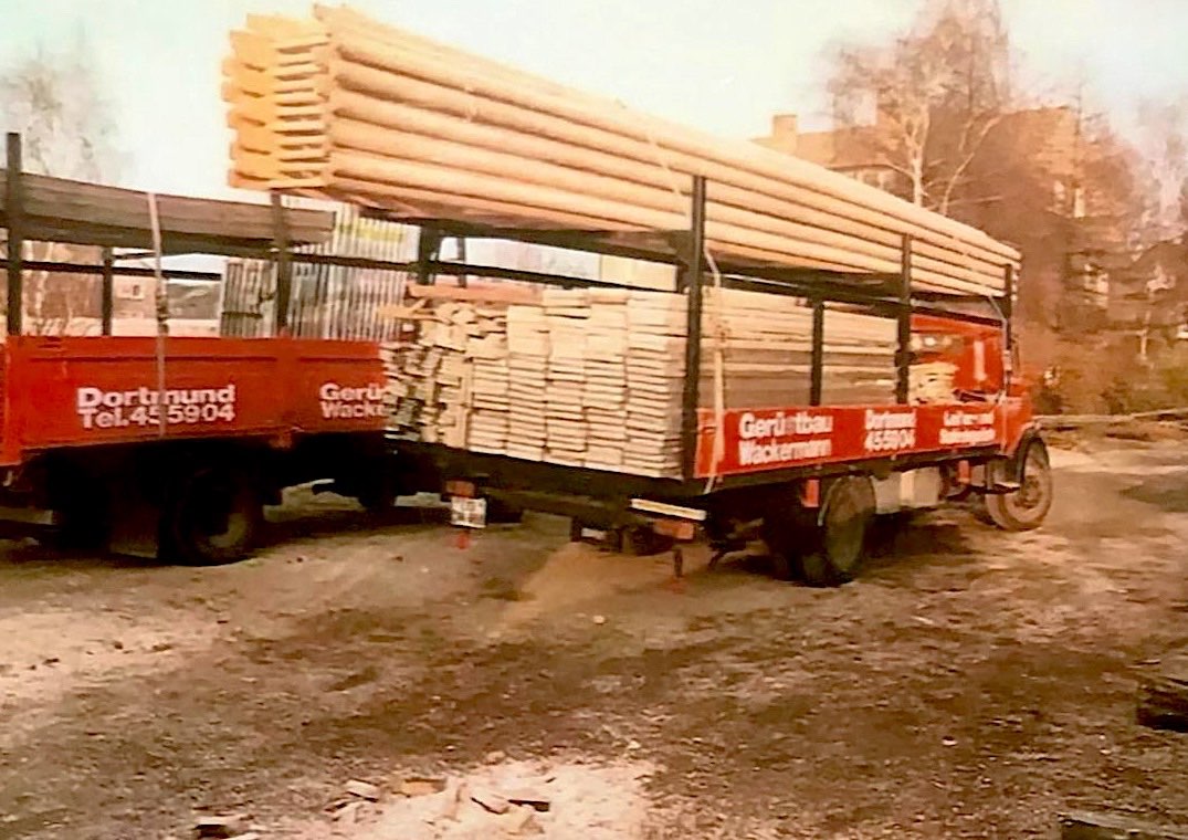 Historisches Foto: roter Wackermann-LKW, beladen mit Leitergerüsten und Bohlen aus Holz